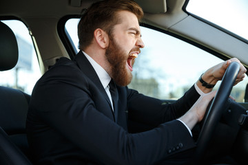 Side view of screaming business man driving and beeps