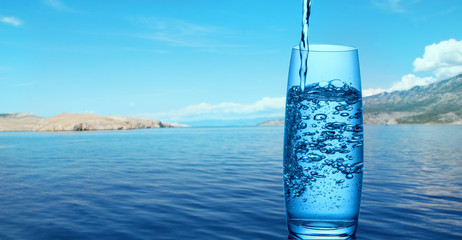 Pouring water into a glass on a background of mountains, sea and nature
