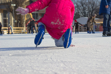 Girl in a red coat and щт blue figured skates fell on  ice rink