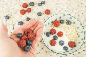 Frau hält in ihrer Hand frische Himbeeren und Blaubeeren, darunter eine Schale mit Müsli, mit Dinkelflocken, Jogurt und Beeren