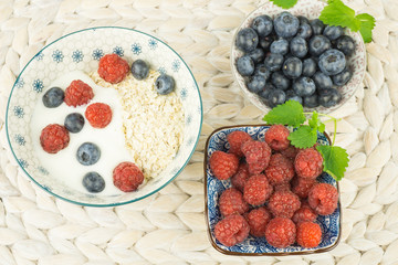 Frisch zubereitetes Müsli mit Beeren, Haferflocken und frischer Milch, daneben eine Schale mit Himbeeren und eine weitere Schale mit Heidelbeeren