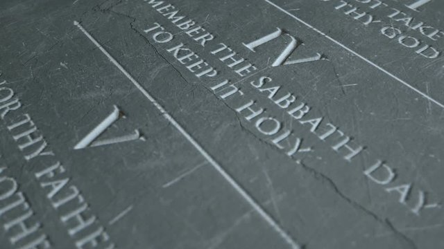 A slow close up pan across a stone tablet with the first five of the ten commandments inscribed onto them