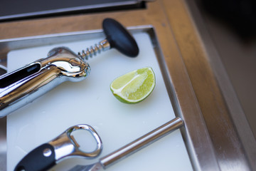 Silver corkscrew, opener and a piece pf lime on a plastic cutting board