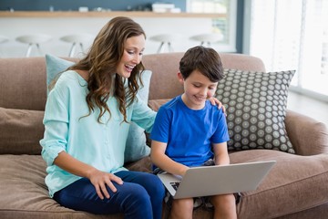 Smiling mother and son sitting on sofa using laptop