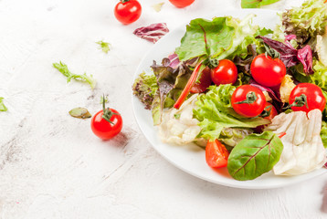 Light salad of green leaves and tomatoes. On a white concrete table, With ingredients, copy space