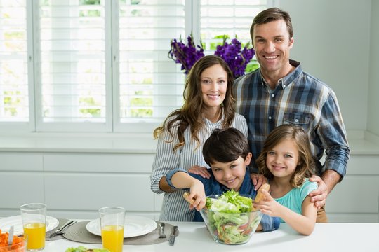 Portrait of smiling family preparing bowl of salad in kitchen