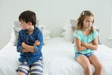 Sad siblings sitting with arms crossed in bedroom