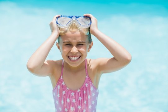 Smiling girl holding her swimming goggles near swimming pool