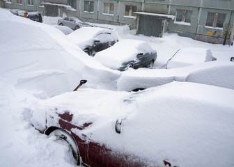 Cars stand in the yard of the house, covered with snow