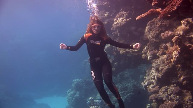 Underwater model free diver swims in clean transparent blue water in Red Sea. Filming a movie. Extreme sport in marine landscape, coral reefs, ocean inhabitants.