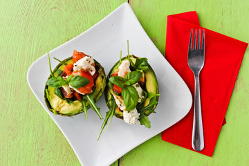 avocado halves with cheese , tomatoes and basil, on green background with red napkin on the side