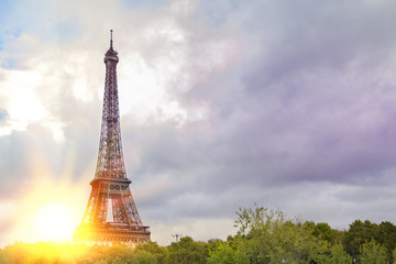 View on Eiffel tower over green summer trees with sunset rays. Beautiful Romantic background. Eiffel Tower from Champ de Mars, Paris, France.