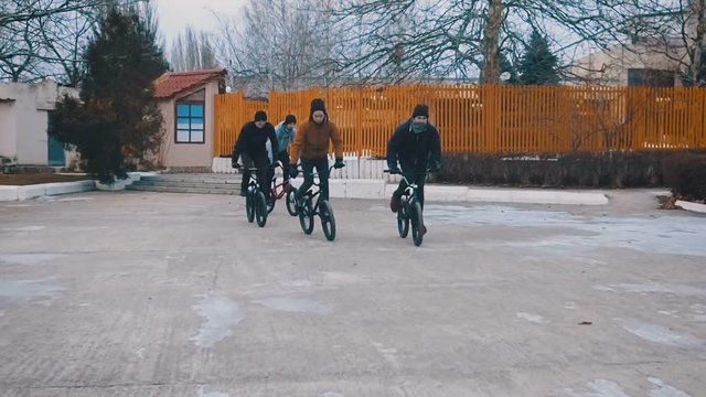 Friends of the teenagers are epically riding together on BMX and doing tricks on a winter day in the park. Slow motion. 120 fps.