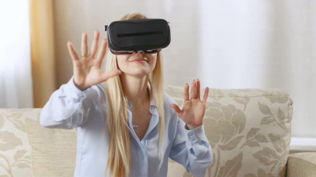 Beautiful Woman in Her Living Room Playing with Virtual Reality Headset. She Gesticulates and Interacts Actively.  Shot on RED EPIC-W 8K Helium Cinema Camera.
