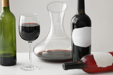 Table with wineglass and bottles of red wine on light background
