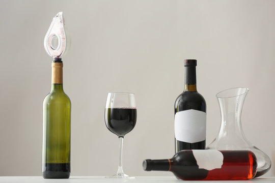 Table with wineglass and bottles of red wine on light background