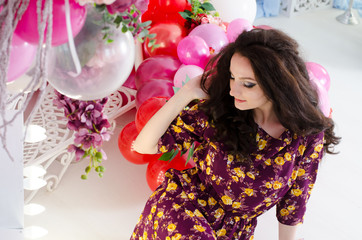 Portrait of a beautiful young woman in a purple floral dress. Sits next to decorative balloons
