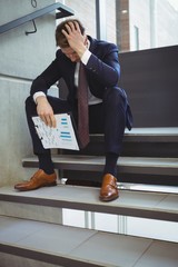 Depressed businessman with clipboard sitting on stairs