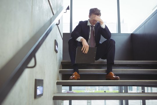 Depressed businessman with clipboard sitting on stairs