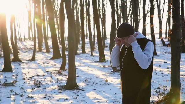 Sports guy with headphones in the park at sunset. Winter jogging in the park. Dark