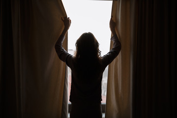 Silhouette of woman closes curtains