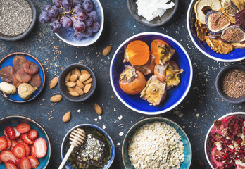 Ingredients in bowls for healthy breakfast over dark blue background, top view. Fresh and dried fruit, chia seeds, oatmeal, nuts, honey. Clean eating, vegan, vegetarian, detox and dieting concept