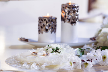 Gold wedding rings on a ivory pillow with a flower. Flames of beautiful white candle at background