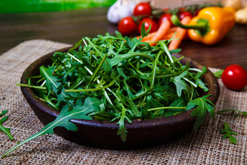 Arugula leaves in bowl. Fresh salad. Pepper and cherry tomatoes. Natural raw vegetables. Organic bio food on rustic wooden table.