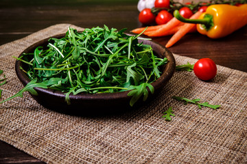 Arugula leaves in bowl. Fresh salad. Carrot, pepper and cherry tomatoes. Natural raw vegetables. Organic bio food on rustic wooden table.