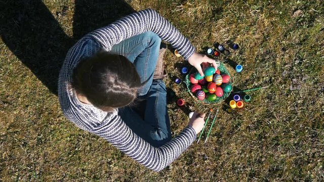Top view of a girl coloring Easter eggs sitting on the grass