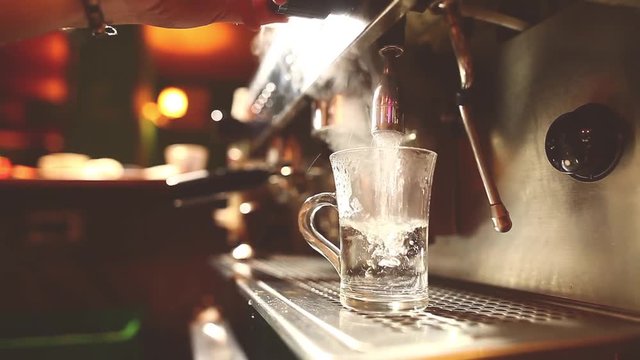 Dolly shot of a barista pouring some boiled water in a transparent cup, in a bar.