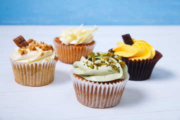 Cupcakes with buttercream. Sweet cake with pistachio cream and small chocolate bar. Dessert on blue wooden background.