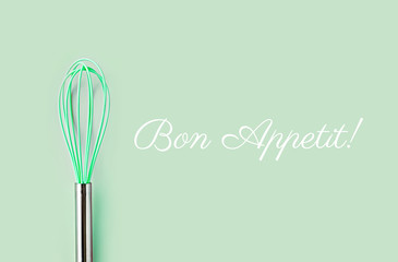 Neon green culinary whisk top view on colorful background. Bon Appetit text. Cook food concept  