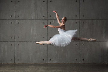 Ballerina in white costume jumping along grey wall in studio © ilyaska