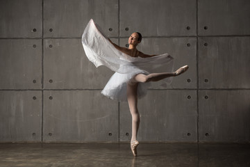 Ballerina dancing with white cloth in studio with grey wall