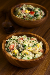 Bunter Quinoa Salat mit Mais, Oliven, Tomaten, Gurken und Schnittlauch in Holzschüssel, fotografiert mit natürlichem Licht (Selektiver Fokus, Fokus in die Mitte des Salats)