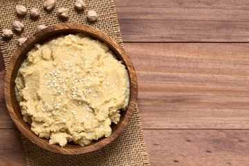 Hummus oder Kichererbsenaufstrich mit Sesam bestreut in Holzschüssel, fotografiert mit...