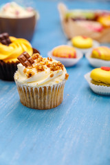 Cupcakes with buttercream and macaroons. Almond macaron cookies. Sweet dessert cakes. On wooden table.