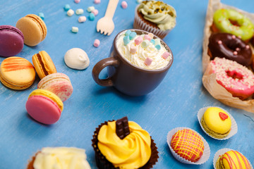 Cupcakes, macaroons and donuts. Mug with whipped cream and marshmallows. Almond macaron cookies. Sweet dessert.