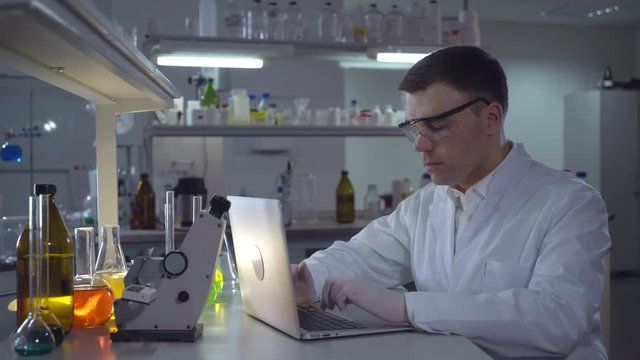 Lab technician entering data on laptop. Professional scientist working with computer in the medical or microbiological laboratory alone. adult focused man chemist engineer wearing in white coat.