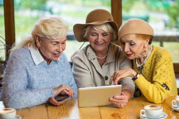 Senior women and tablet. Three ladies at cafe table. Find friends in social network. - Powered by Adobe