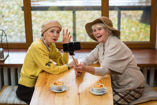 Senior ladies taking selfie. Elderly women beside cafe window. How to use monopod.