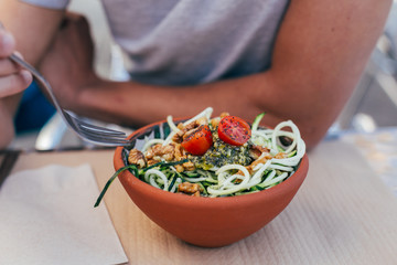 Young man eats a vegan zoodles with pesto and vegetables