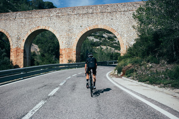 Fototapeta na wymiar Professional cyclist riding toward a bridge in Spanish summer sunlight