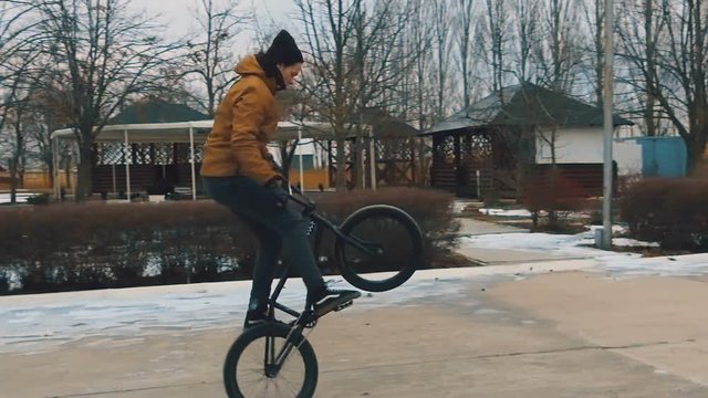 Teenager rides the BMX and does tricks and jumps in the winter park. Slow motion. 120 fps.