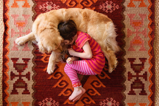 Overhead view of girl lying on floor with a golden retriever dog