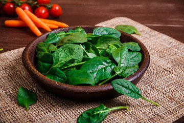 Spinach leaves in bowl. Carrot and cherry tomatoes. Raw fresh vegetable. Fresh natural plant leaf. Organic bio food on rustic wooden table.