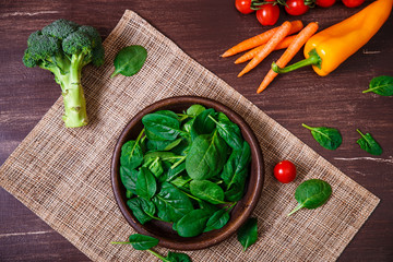 Spinach leaves in bowl. Carrot, pepper and cherry tomatoes, brocoli. Raw fresh vegetable. Fresh natural plant leaf. Organic food on wooden table.