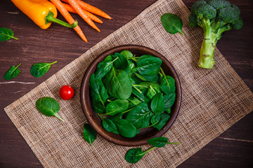 Spinach leaves in bowl. Carrot, pepper and cherry tomatoes, brocoli. Raw fresh vegetable. Fresh natural plant leaf. Organic food on wooden table.