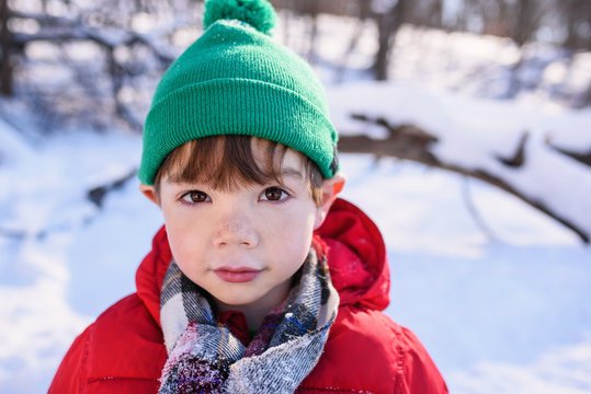Close-up Portrait of a young boy standing a snowy garden wearing a bobble hat pushing his ears out to look like an elf